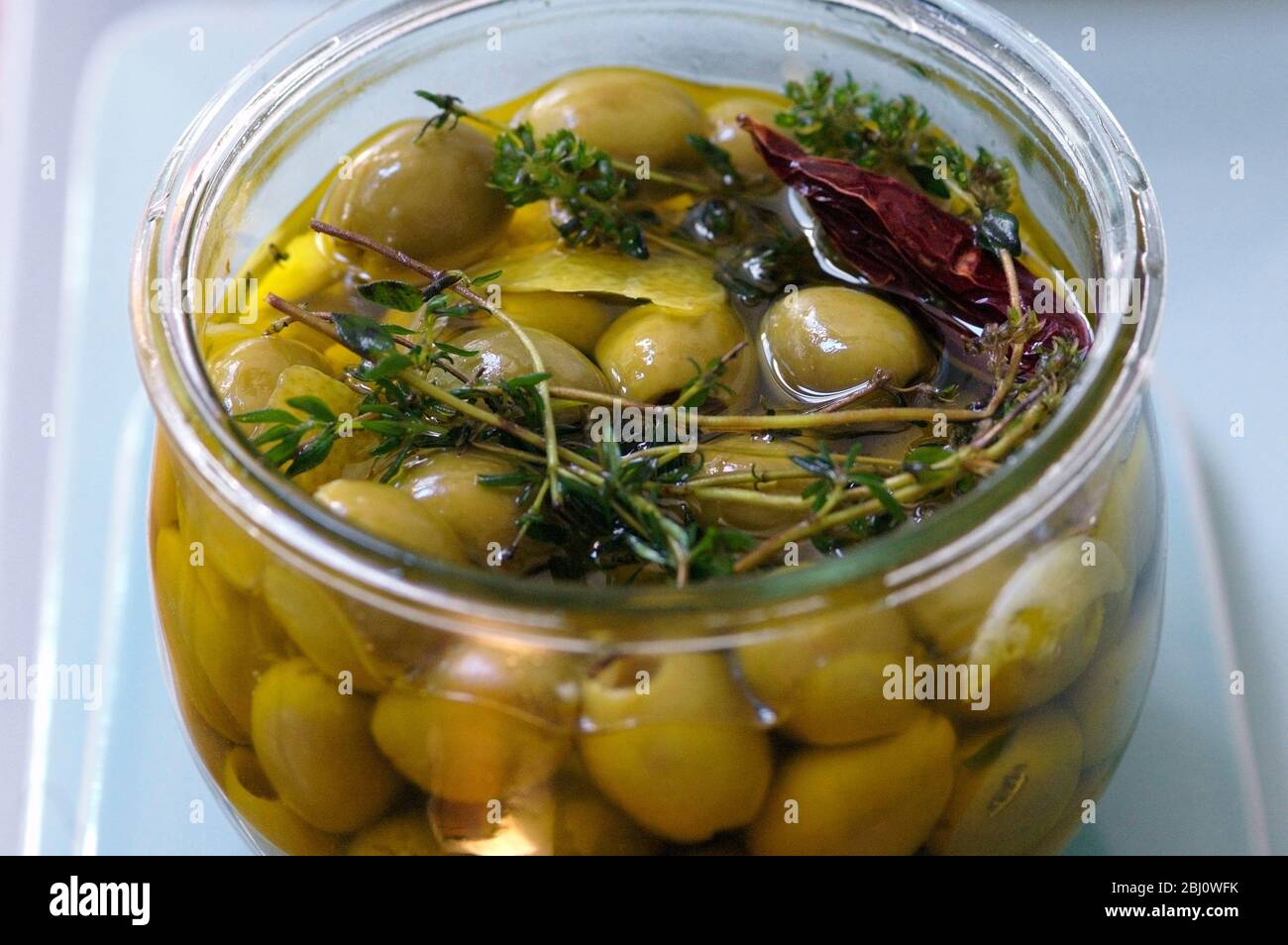 Olive verdi snocciolate marinate in olio d'oliva vergine aromatizzate con ciuffi di timo, scorza di limone e peperoncino Foto Stock