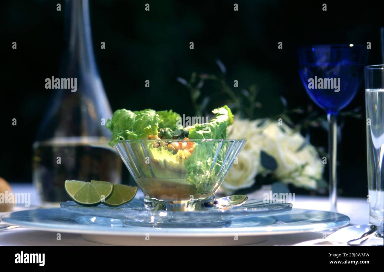 Insalata di aragosta servita in foglie di lattuga in una ciotola di vetro di cristallo in un ambiente formale da tavolo all'aperto pranzo partito estivo, con rose e vino bianco - Foto Stock