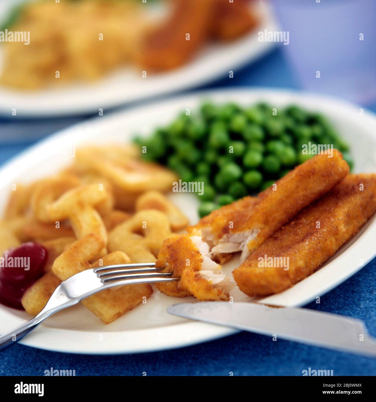 Cod dita di pesce sul piatto del bambino con scaglie di alfabeto e piselli verdi e ketchup di pomodoro - Foto Stock