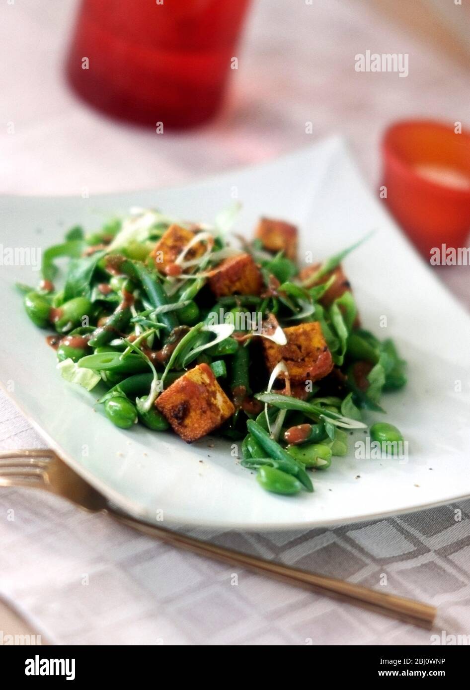 Insalata vegetariana di tofu fritto con fave, fagioli francesi, cipolle primaverili, cipolle, su piatto bianco quadrato - Foto Stock