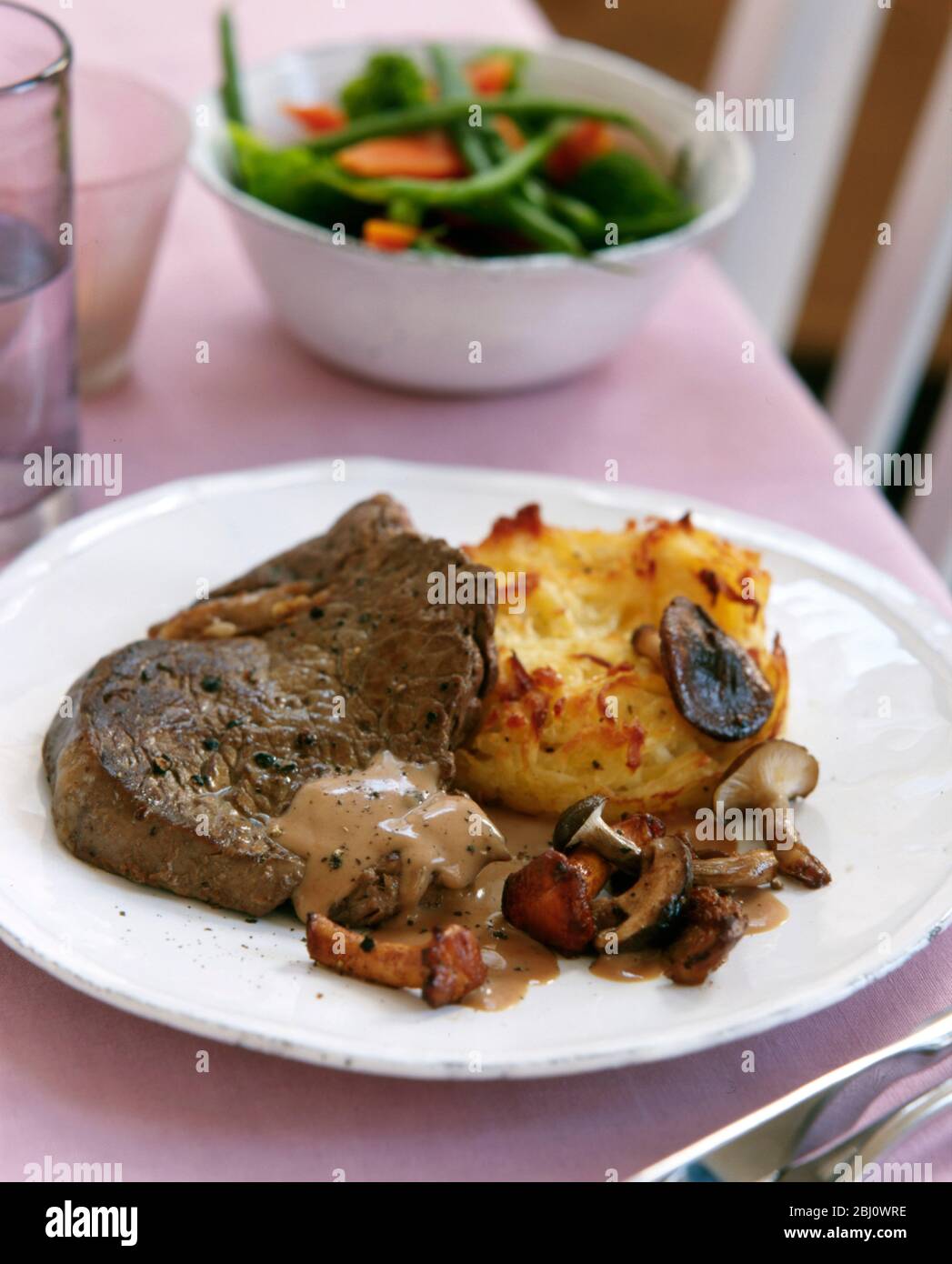 Porzione di bistecca alla griglia con funghi e patate arrosto su piatto bianco - Foto Stock