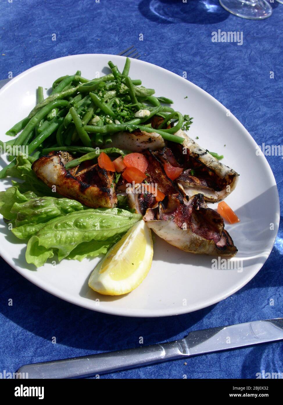 Insalata di calamari alla griglia con pomodoro a dadini, fagioli verdi e lattuga con piatto bianco di limone al ristorante all'aperto vicino al mare a Menton, a sud di Foto Stock