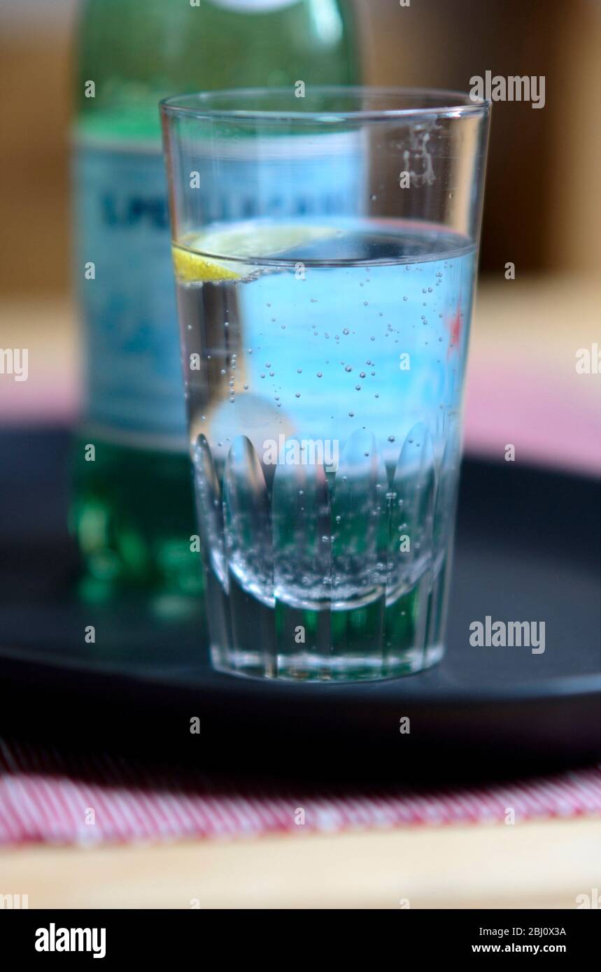 Bicchiere di Pellegrino leggermente frizzante, acqua minerale italiana, con un piccolo spicchio di limone su vassoio scuro - Foto Stock