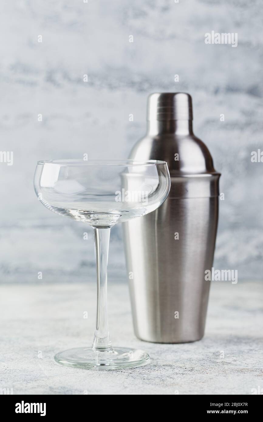 Svuotare il bicchiere di champagne largo e lo shaker in metallo su sfondo chiaro. Set di piatti per preparare cocktail Foto Stock