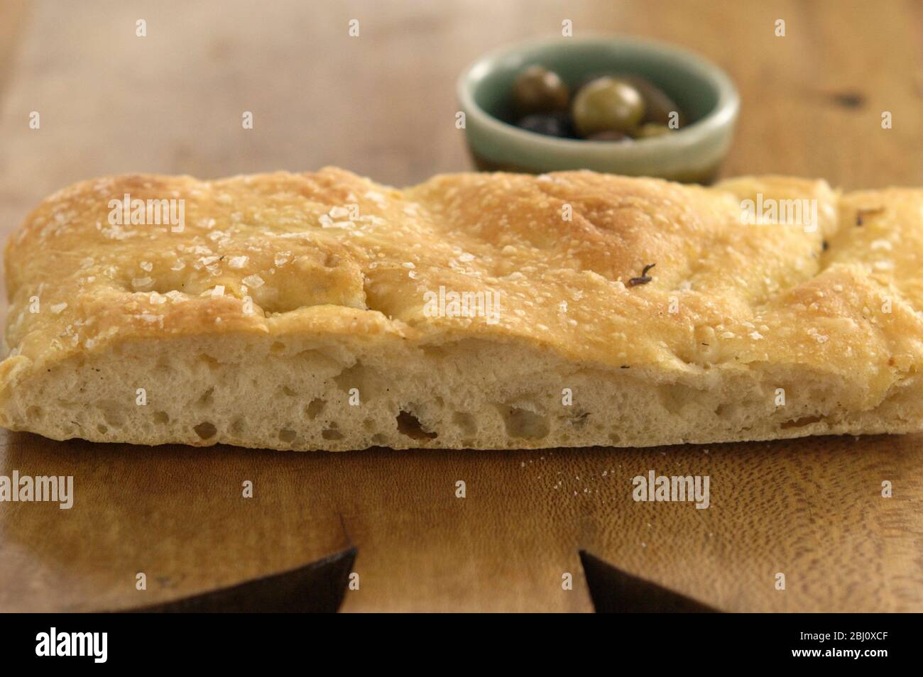 Focaccia all'olio d'oliva e al rosmarino su tavola di legno con ciotole di olio d'oliva e olive intere. - Foto Stock