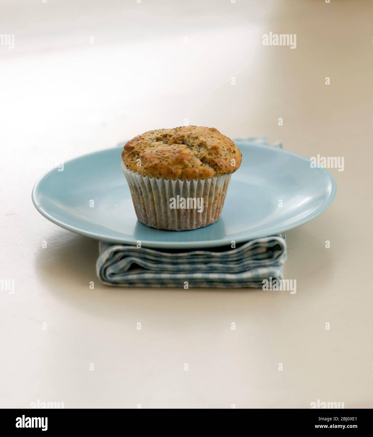 Muffin a semi di papavero singolo su piastra blu su tovagliolo di controllo, su tavola dipinta. - Foto Stock