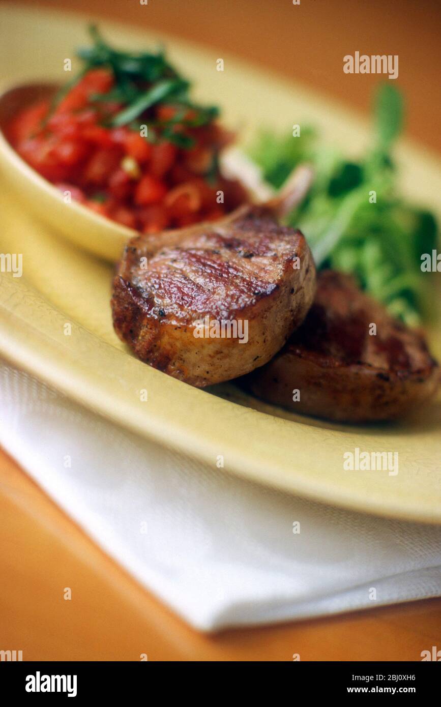 Costolette di agnello alla griglia con salsa di pomodoro e insalata su piatto di glassa di crackle giallo - Foto Stock