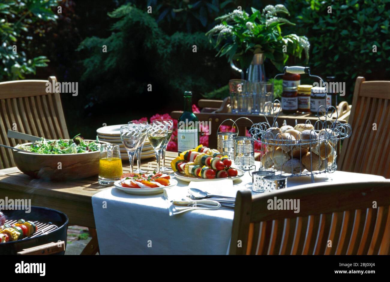 Elegante barbecue tavolo pranzo fuori al sole, insalata in grande ciotola di legno, insalata di pomodoro e mozzarella, kebab di verdure, condimento olio d'oliva, pane r Foto Stock