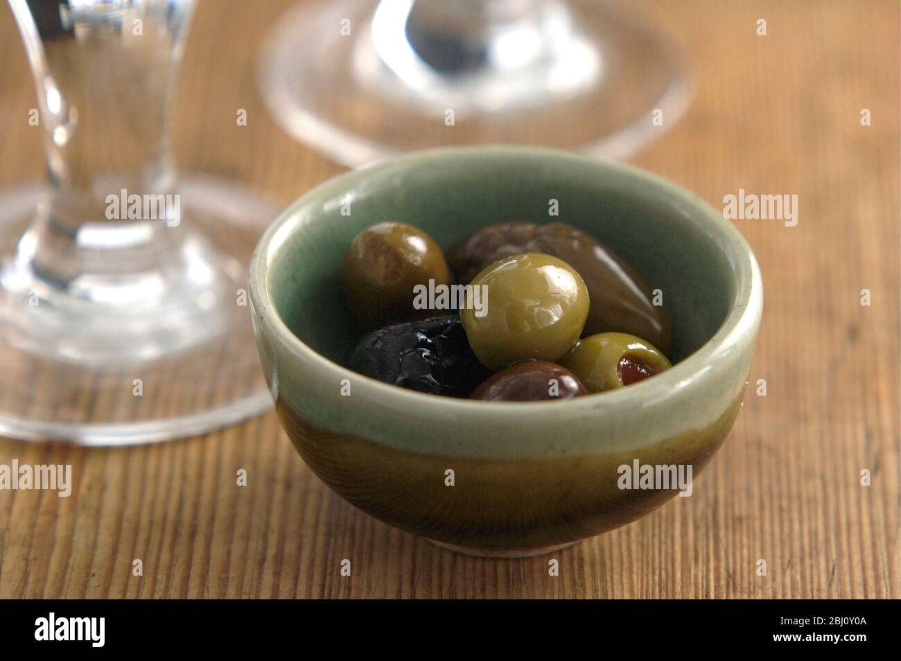 Olive italiane in piccola ciotola in ceramica su una superficie rustica in legno con basi di bicchieri da vino - Foto Stock