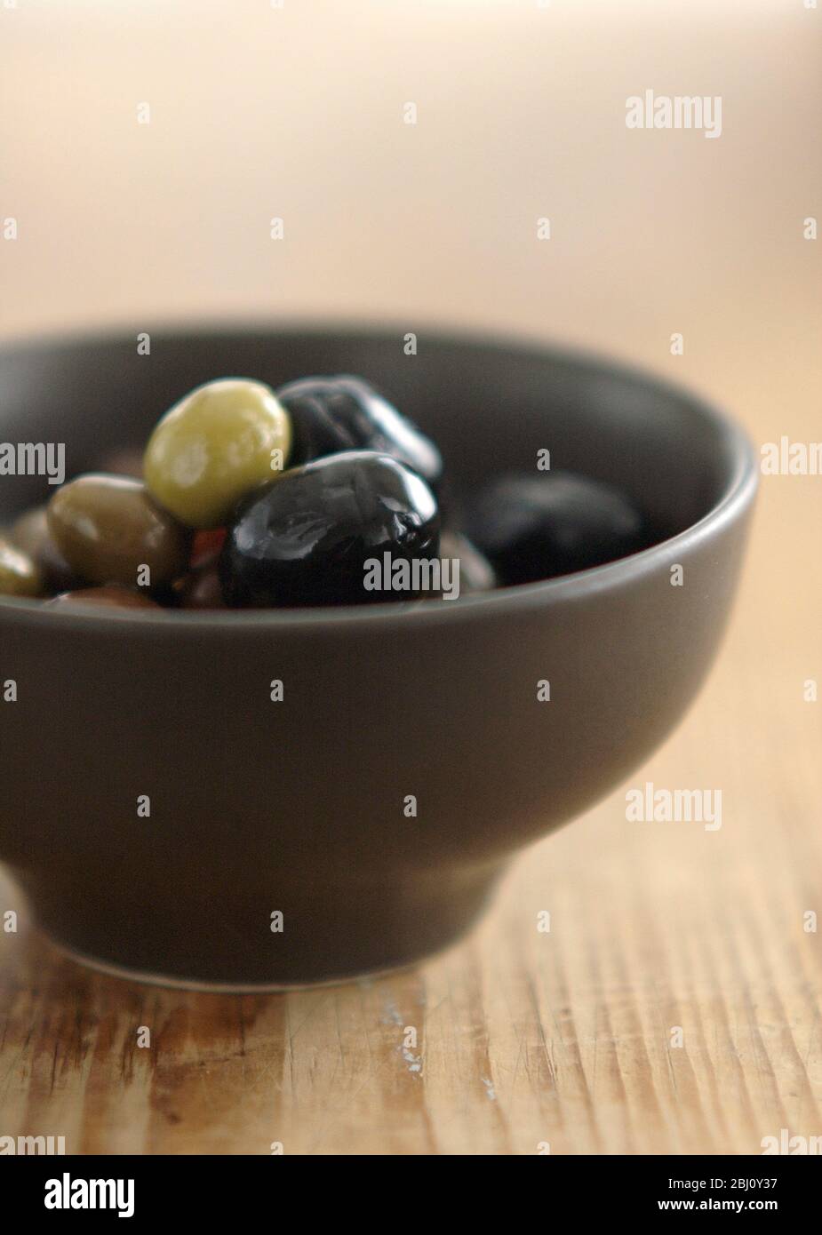 Olive italiane miste in piccola ciotola di ceramica su superficie rustica in legno - Foto Stock