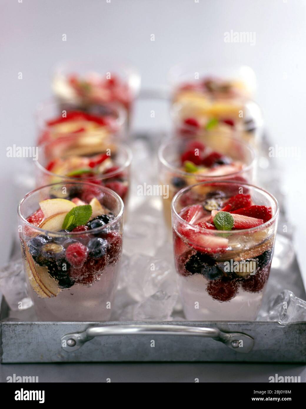 Otto bicchieri di frutta fresca e acqua minerale frizzante su metallo, vassoio pieno di ghiaccio - Foto Stock