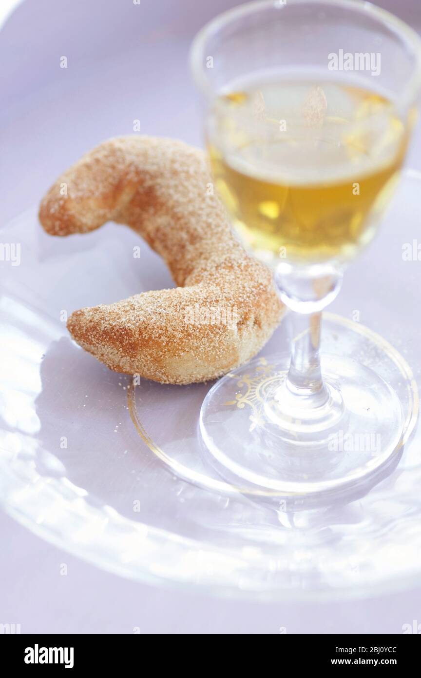 Biscotto a forma di mezzaluna con bicchiere di vino da dessert su piatto di vetro - Foto Stock