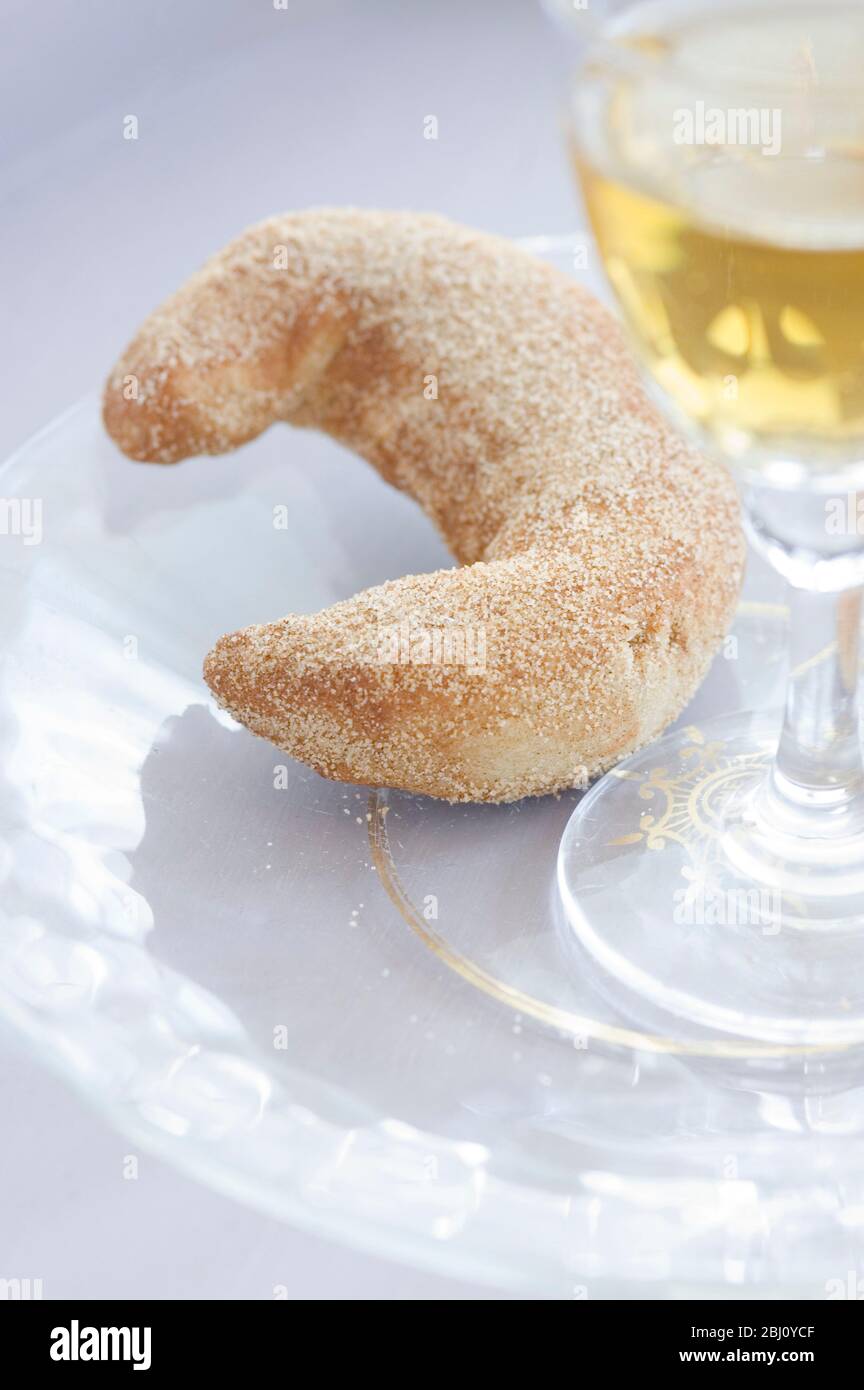 Biscotto a forma di mezzaluna con bicchiere di vino da dessert su piatto di vetro - Foto Stock