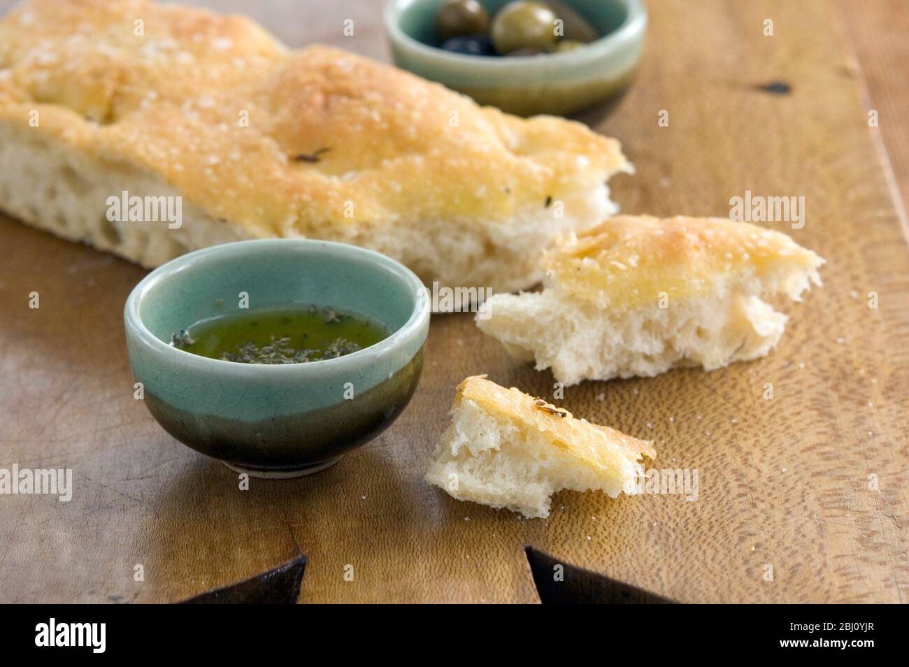 Focaccia all'olio d'oliva e al rosmarino su tavola di legno con ciotole di olio d'oliva gregge e olive intere - Foto Stock