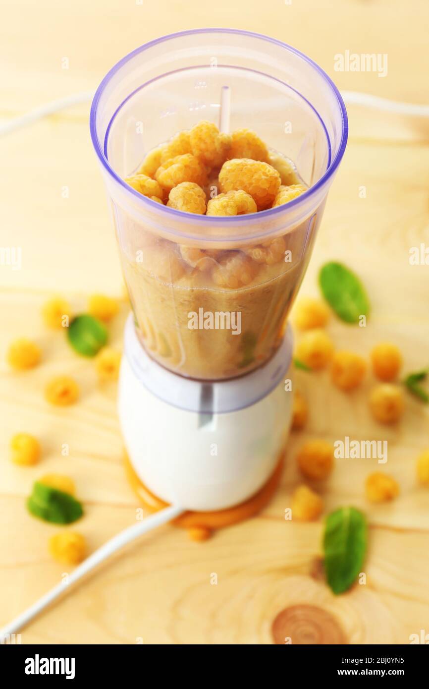 Lamponi gialli in tazza frullatore su tavolo di legno, primo piano Foto Stock