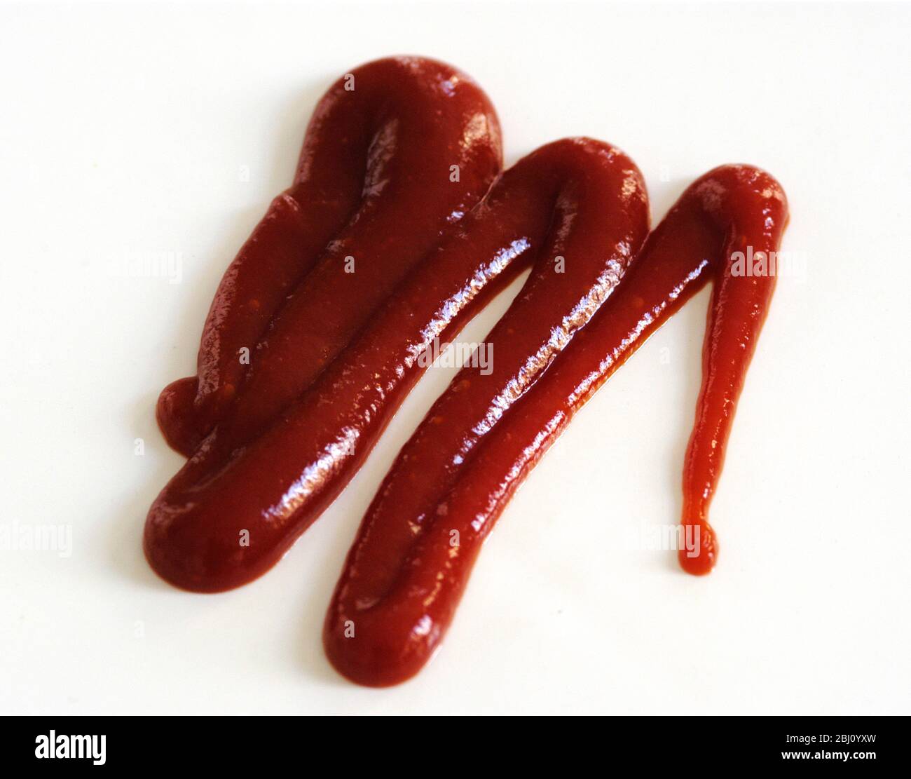 Squiggle di ketchup di pomodoro spremuto da squeezy bottiglia su sfondo bianco - Foto Stock