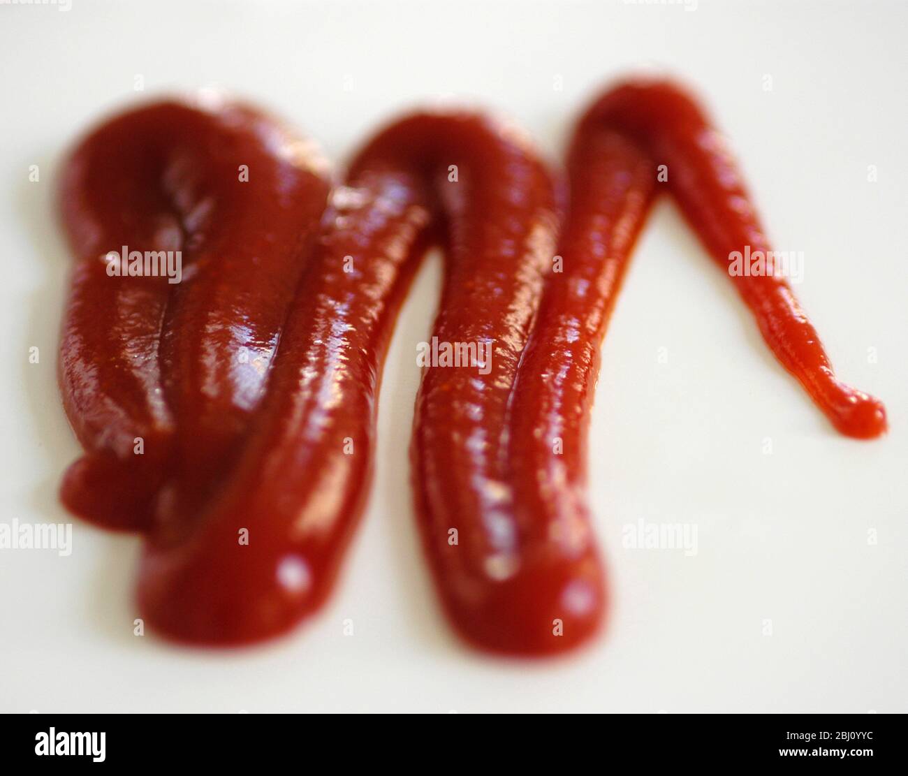 Squiggle di ketchup di pomodoro spremuto dalla bottiglia squeezy su sfondo bianco. - profondità di campo molto breve - Foto Stock