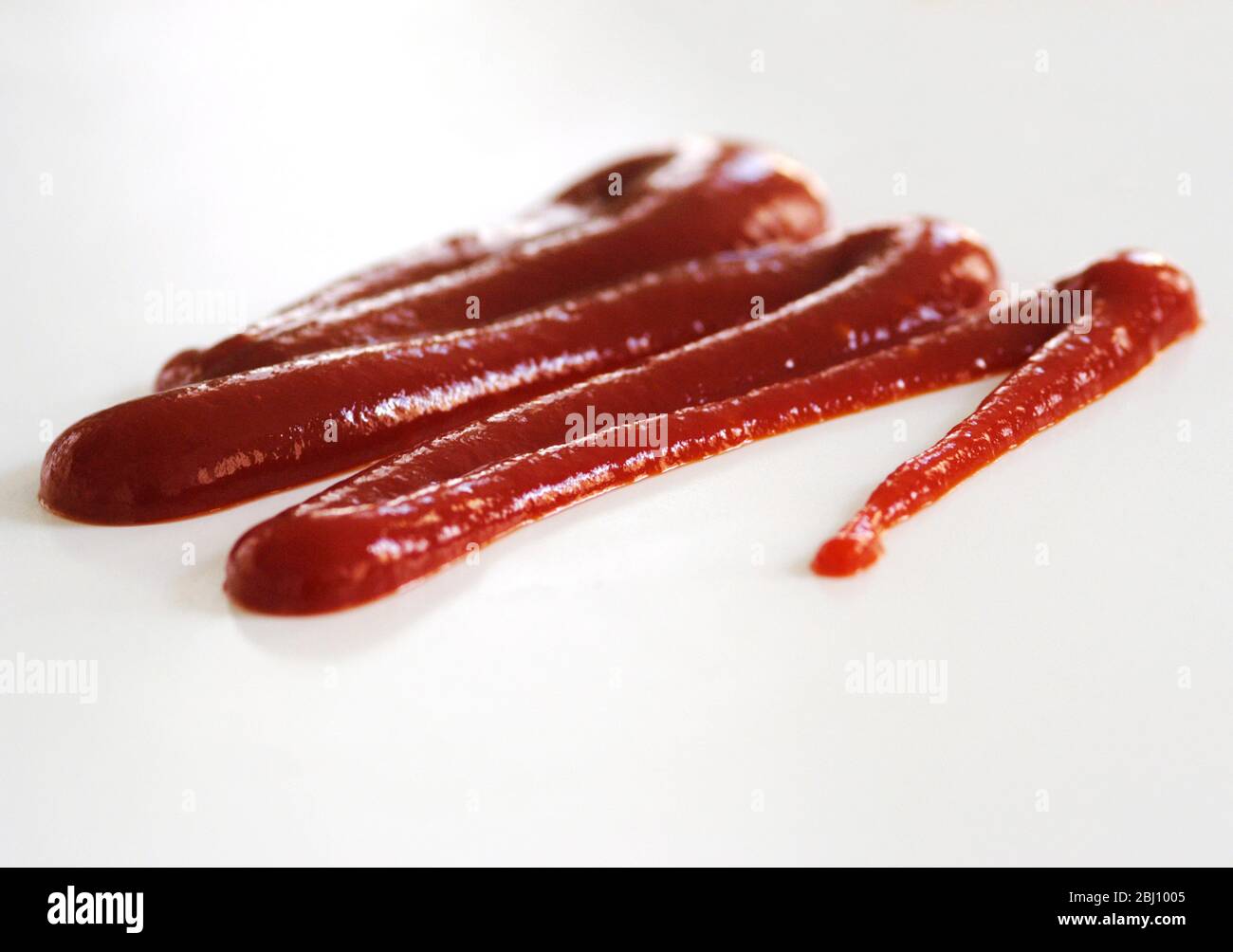 Squiggle di ketchup di pomodoro spremuto da squeezy bottiglia su sfondo bianco - Foto Stock