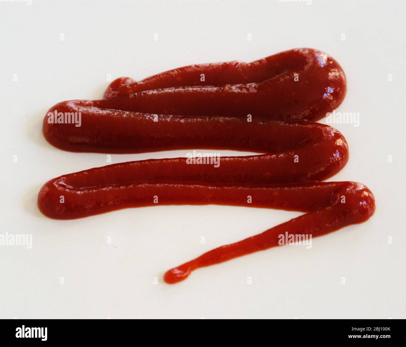 Squiggle di ketchup di pomodoro spremuto da squeezy bottiglia su sfondo bianco - Foto Stock