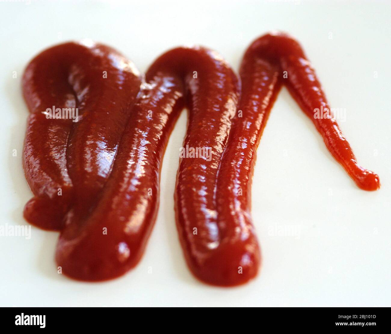 Squiggle di ketchup di pomodoro spremuto da squeezy bottiglia su sfondo bianco - Foto Stock