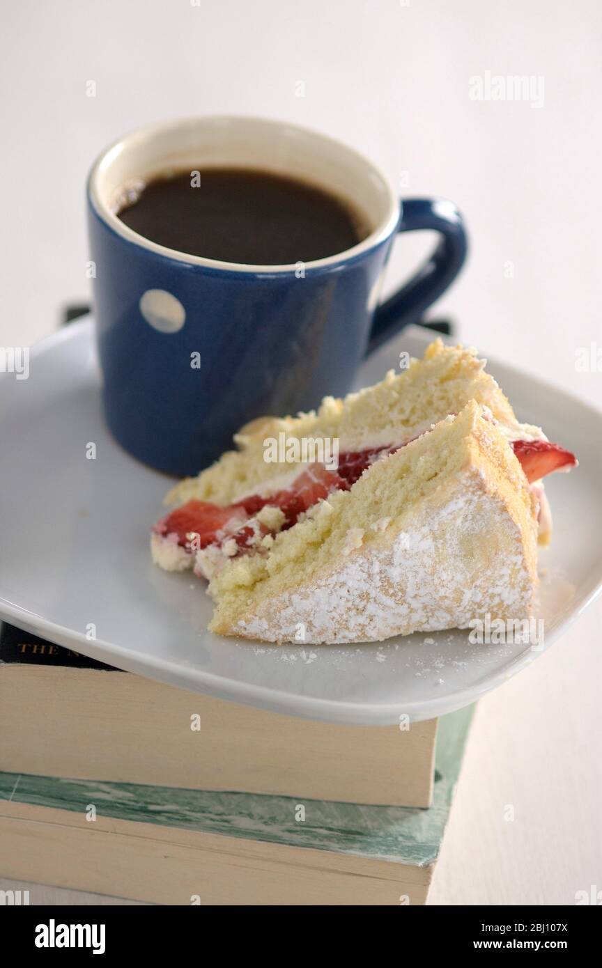 Un pezzo di torta di Spagna di fragola su un piatto bianco con una piccola tazza macchiata blu e bianca di caffè nero - Foto Stock