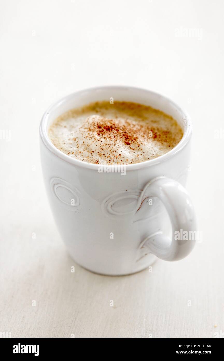 Tazza bianca di caffè cappuccino con aggiunta di schiuma e polvere di cacao spruzzata su - Foto Stock