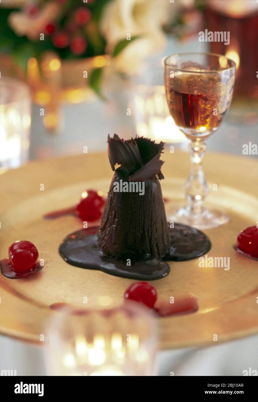 Parfait di ghiaccio coperto al cioccolato su piatto d'oro con ciliegie e bicchiere di vino da dessert sul tavolo natalizio - Foto Stock
