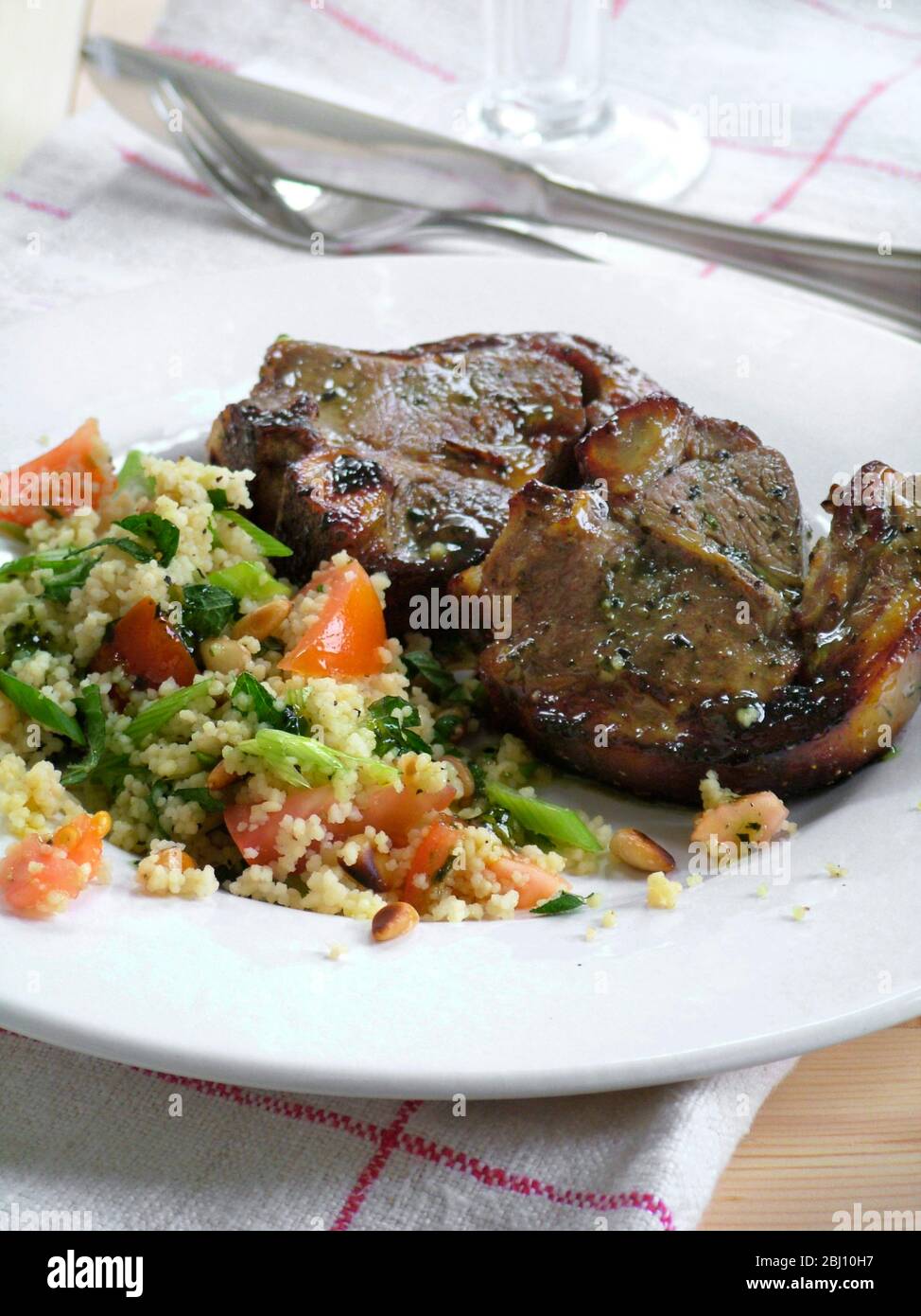 Due costolette di agnello con couscous con verdure su piatto bianco - Foto Stock