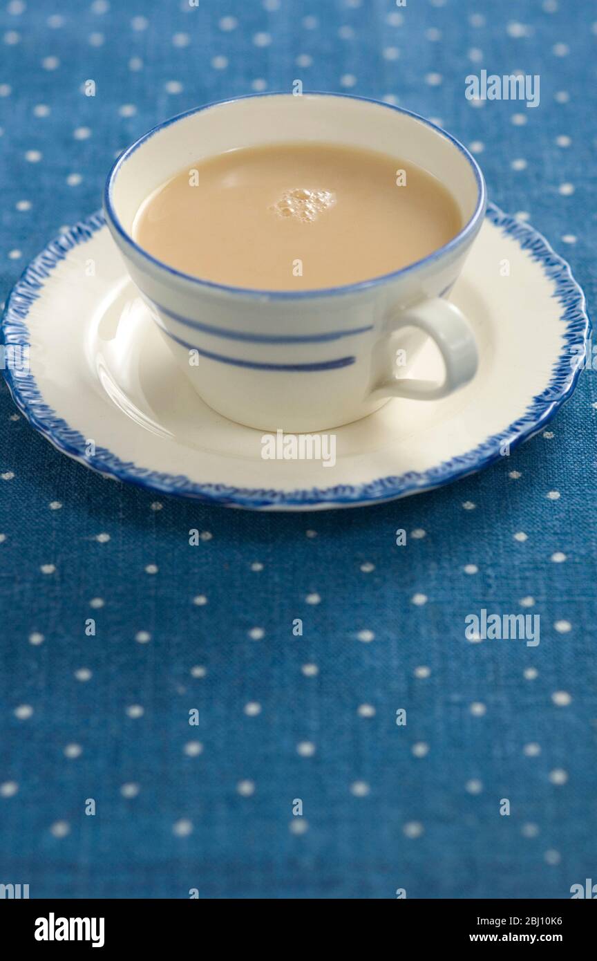 Tazza e piattino blu e crema di porcellana con tè lattiginoso, su panno da tavolo macchiato. - Foto Stock