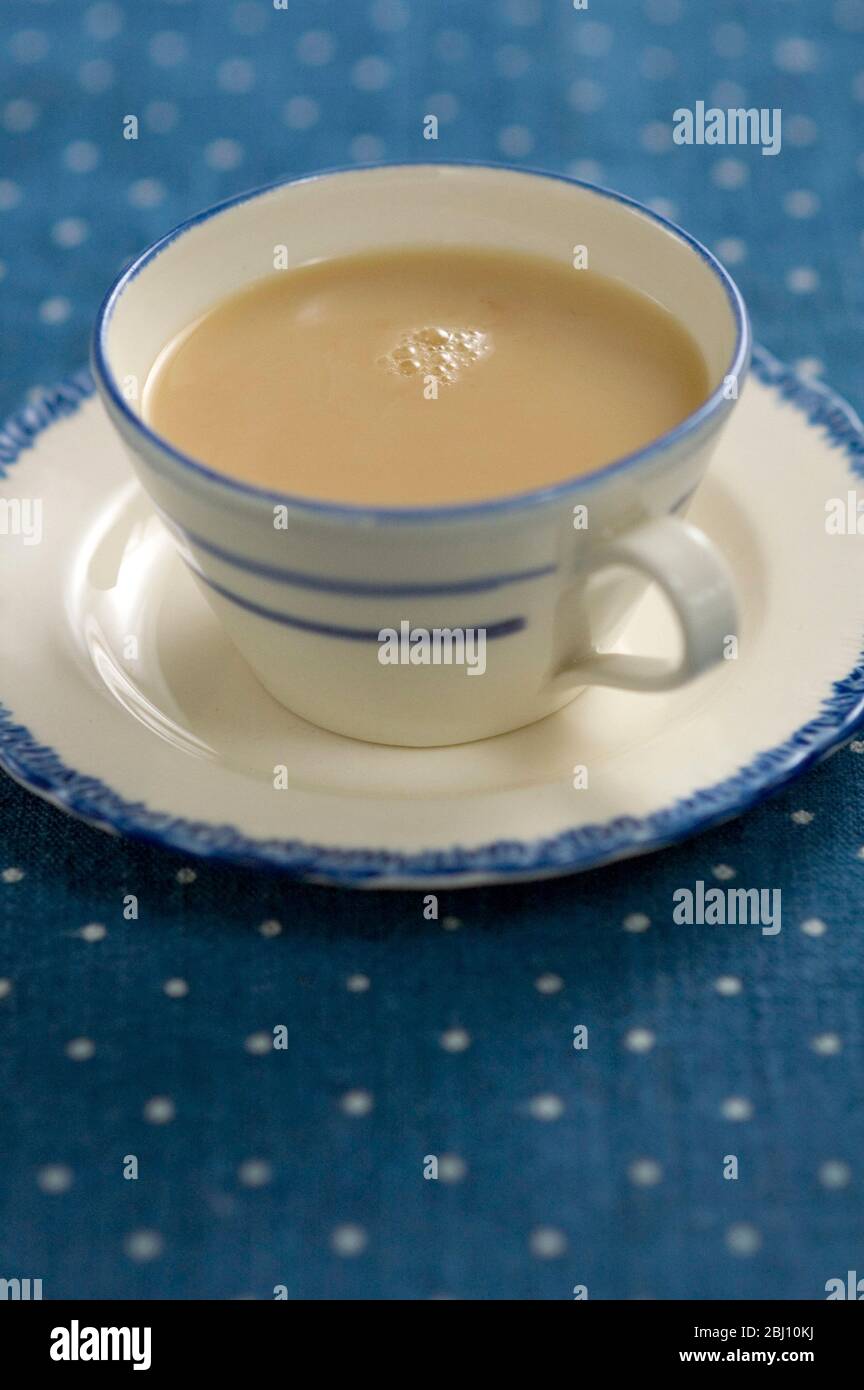 Tazza e piattino blu e crema di porcellana con tè lattiginoso, su panno da tavolo macchiato. - Foto Stock