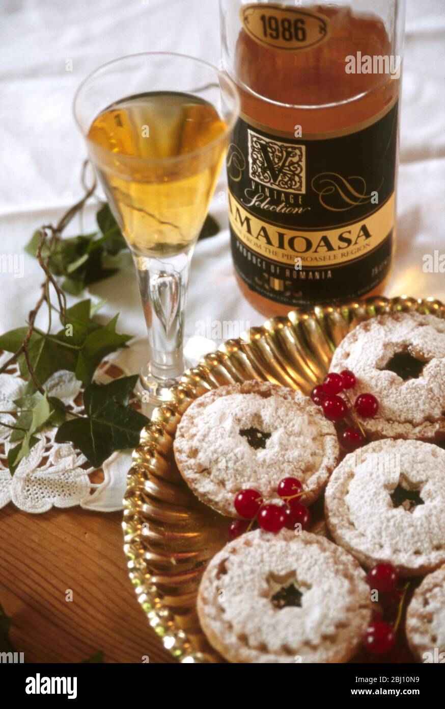 Piatto d'oro con torte di natale con vino da dessert in bicchiere e rametto di edera - Foto Stock