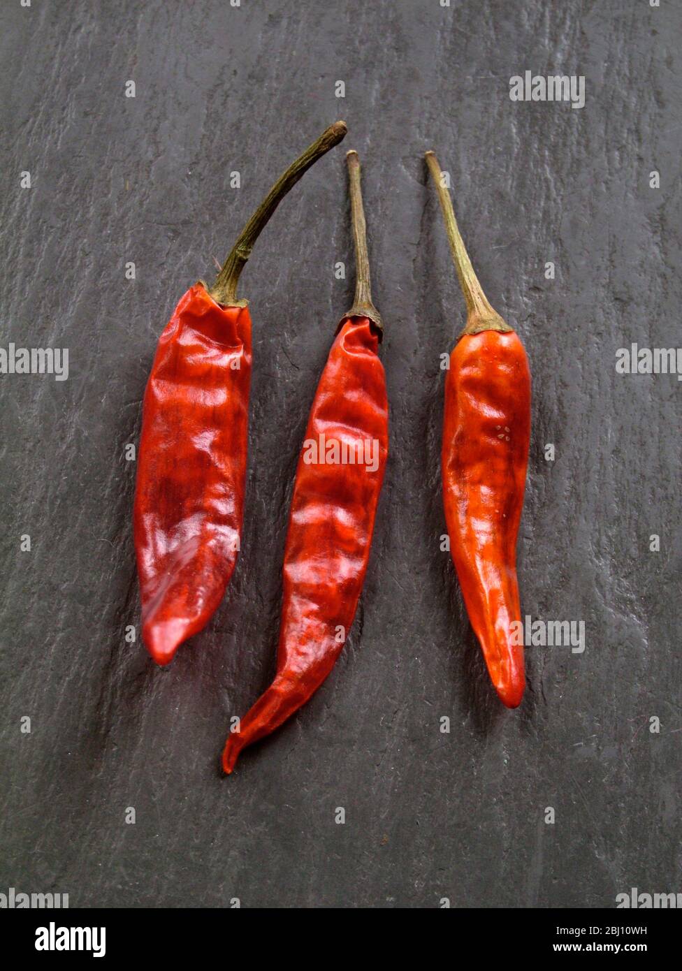 Tre peperoncini rossi caldi semi-essiccati su ardesia grigia - Foto Stock