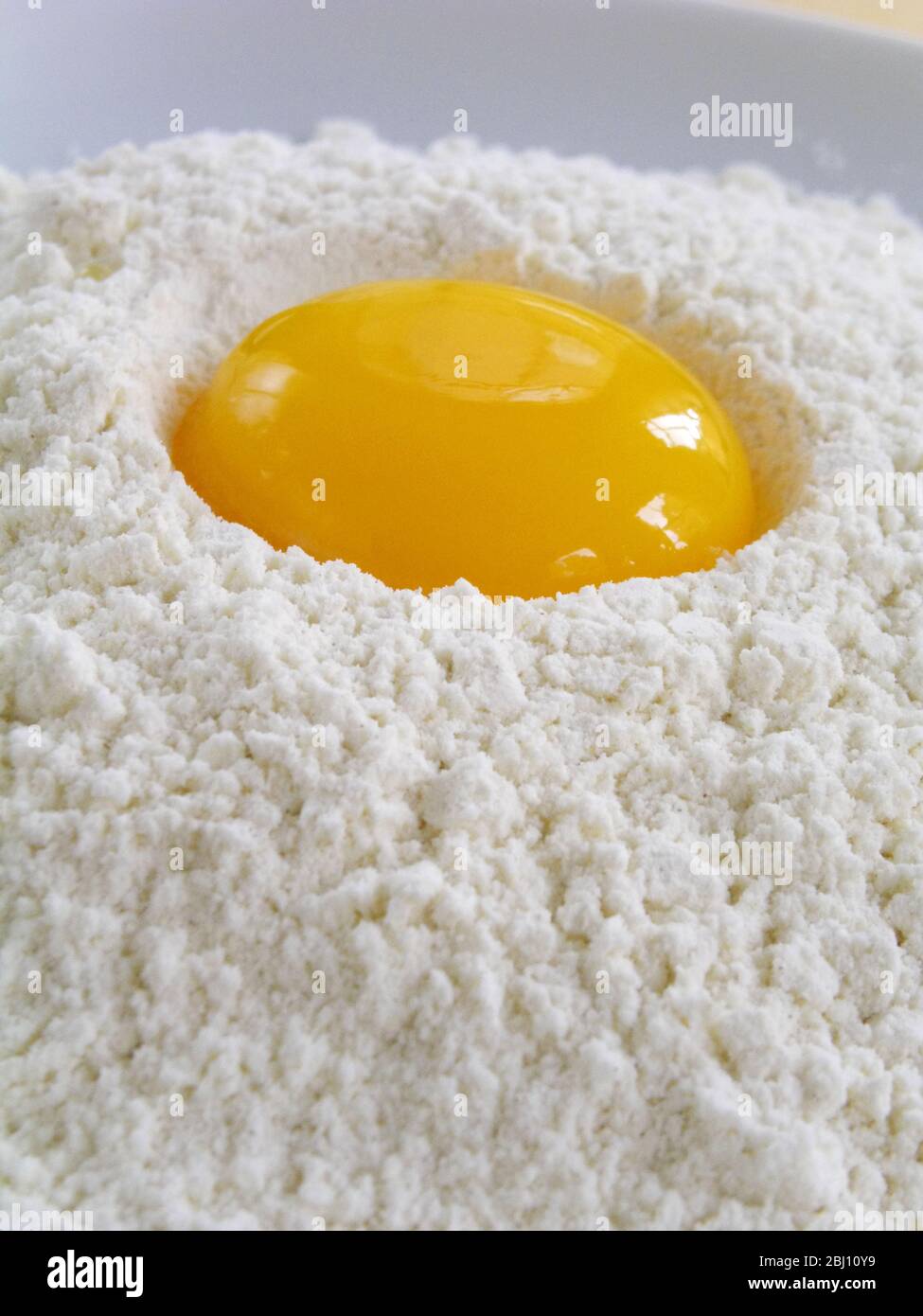 Un tuorlo d'uovo intero spezzato in un mucchio di farina setacciata - Foto Stock
