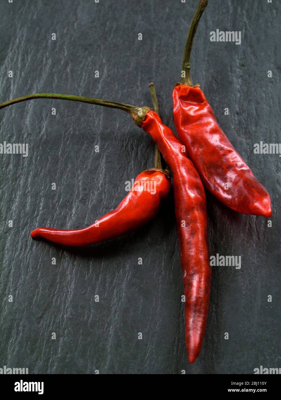 Tre peperoncini rossi caldi semi-essiccati su ardesia grigia - Foto Stock