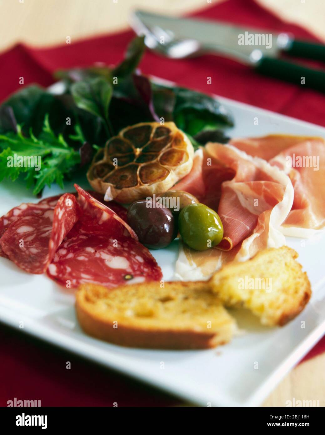 Antipasti di salame, prosciutto di parma, olive, aglio arrosto, foglie di insalata e pane tostato con olio d'oliva - Foto Stock