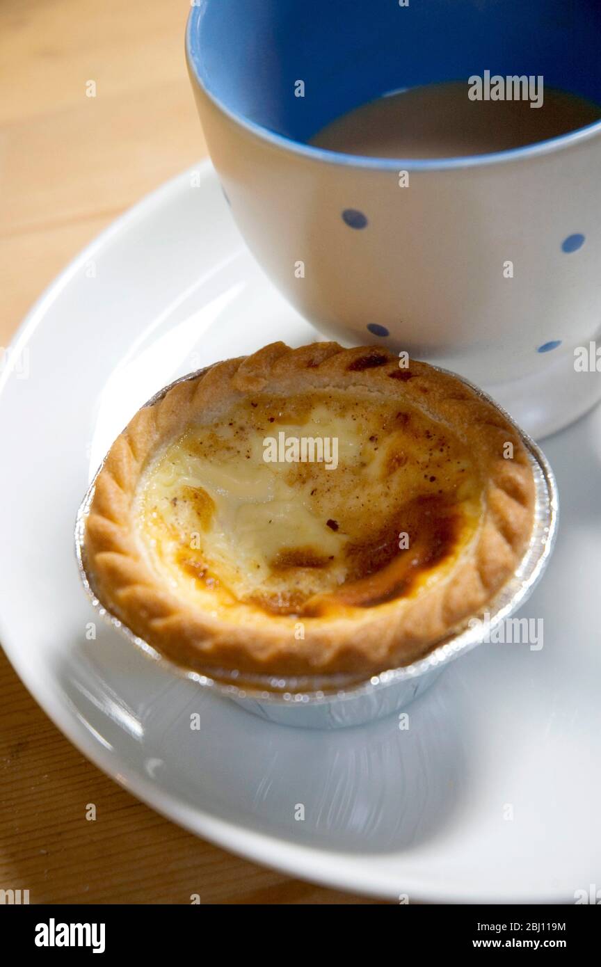 Crostata di crema acquistata da panettieri con tazza di tè su piatto bianco - Foto Stock