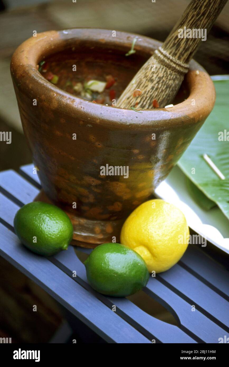 Intonando insieme gli ingredienti per un curry tailandese in un grande pestello rustico con mortaio - Foto Stock