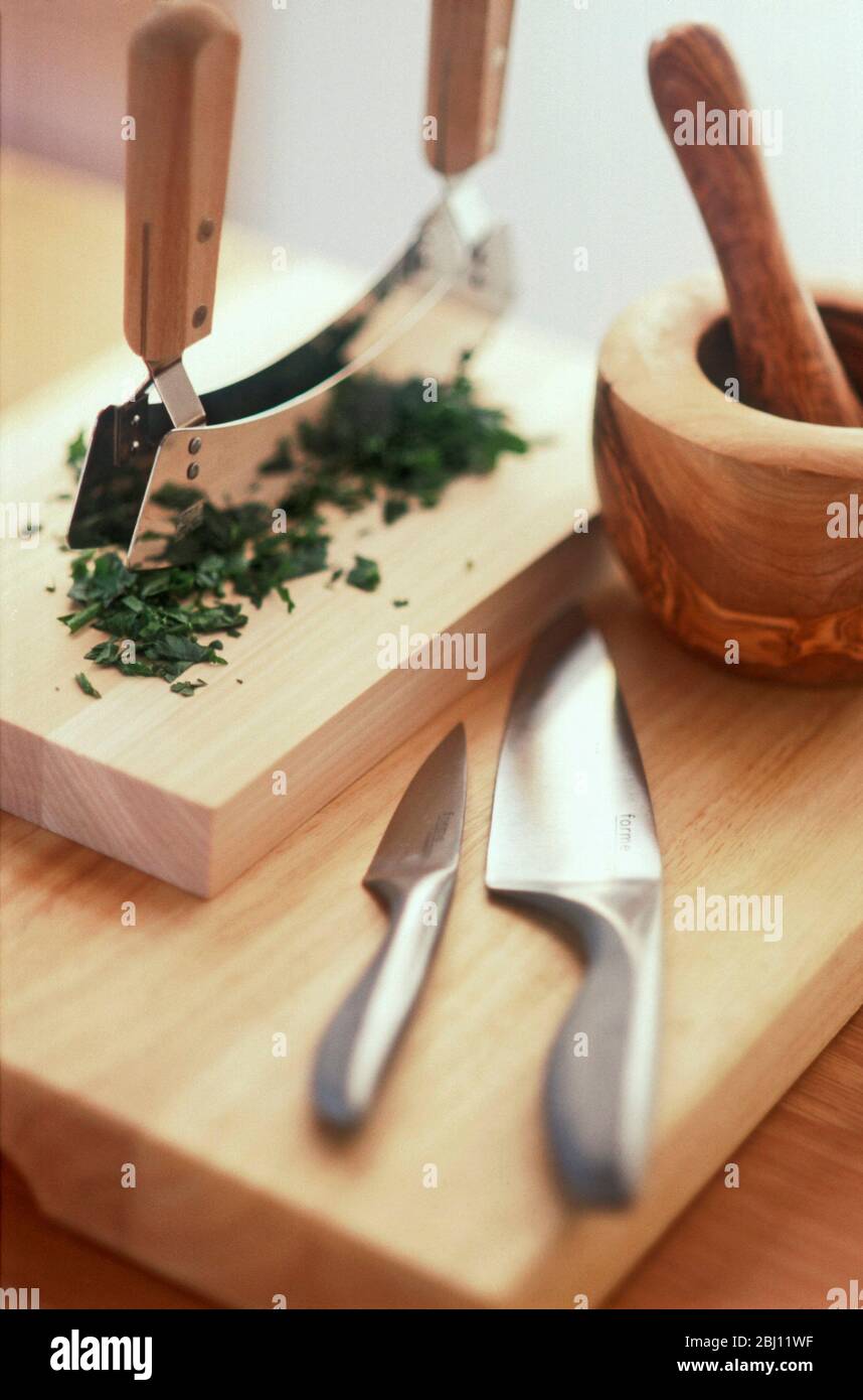 Usando la doppia semiluna per acquistare erbe su moderno legno con pestello e mortaio di legno per tritare loro - Foto Stock