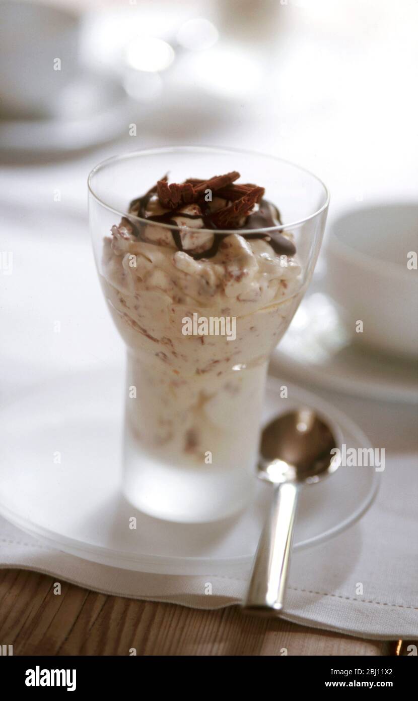 Dessert al cioccolato e alla crema in moderno vetro su piccolo piatto di vetro in tavolo - Foto Stock