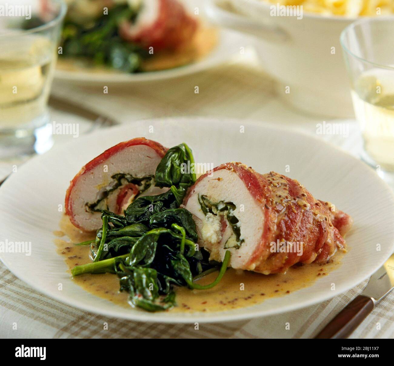 Piatto di filetto di pollo avvolto nel prosciutto di parma e servito con spinaci appassiti - Foto Stock