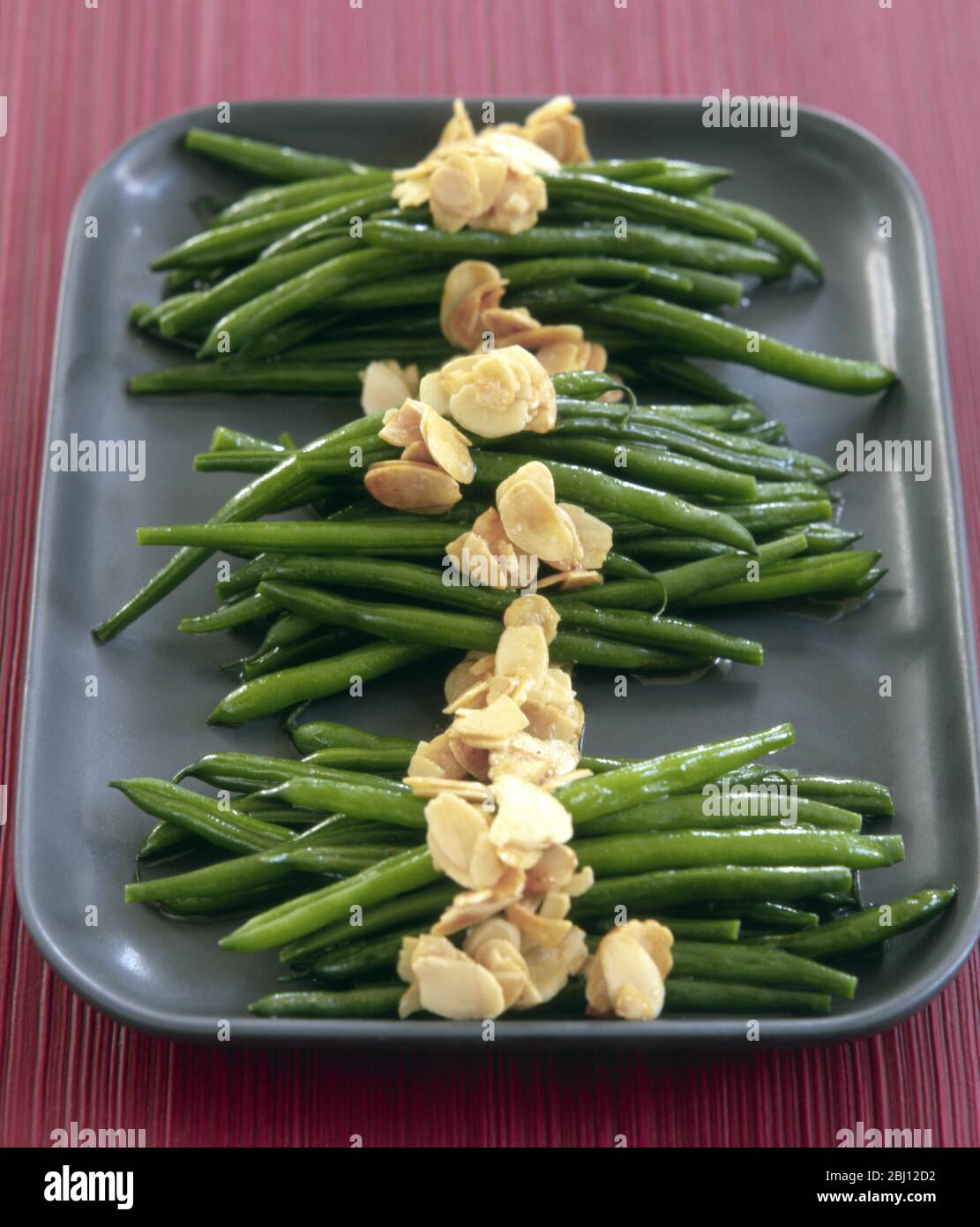 Fagioli verdi formalmente disposti su piatto grigio con mandorle tostate - Foto Stock