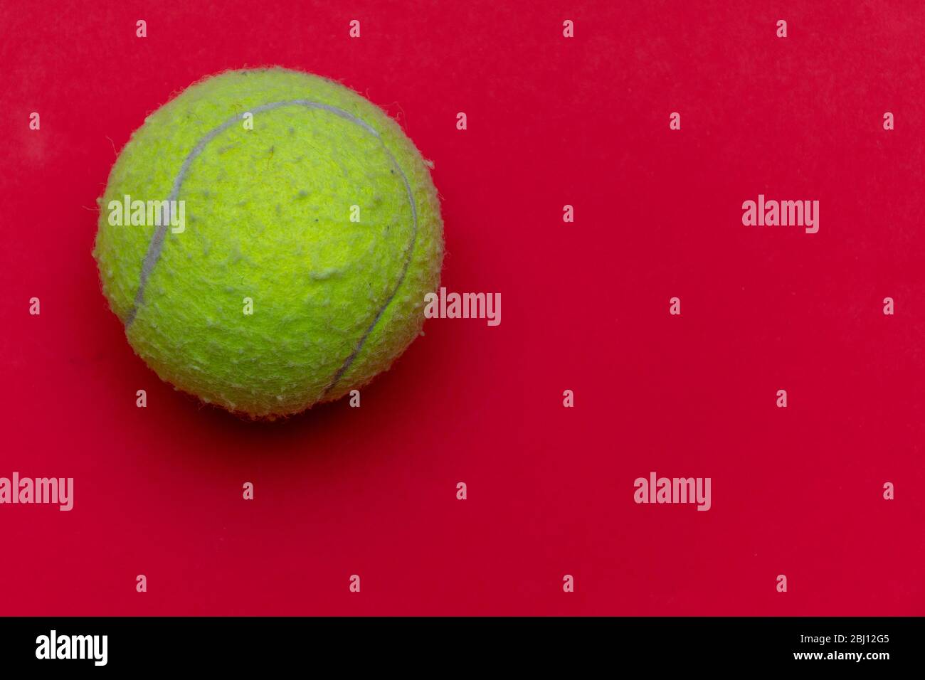 Palla da tennis giallo brillante su un solido rosso brillante e piatto sfondo simboleggia sport e attività con spazio copia. Foto Stock
