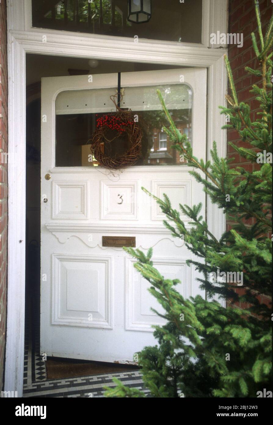Porta anteriore socchiusa al periodo di Natale - albero esterno e corona appesa alla porta - - Foto Stock