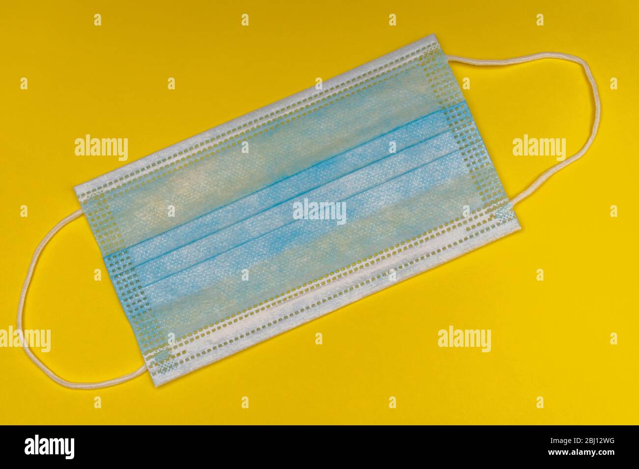 Maschera medica blu, piatta su sfondo giallo brillante per la prevenzione della cura della salute e precauzioni COVID-19 (Coronavirus). Foto Stock