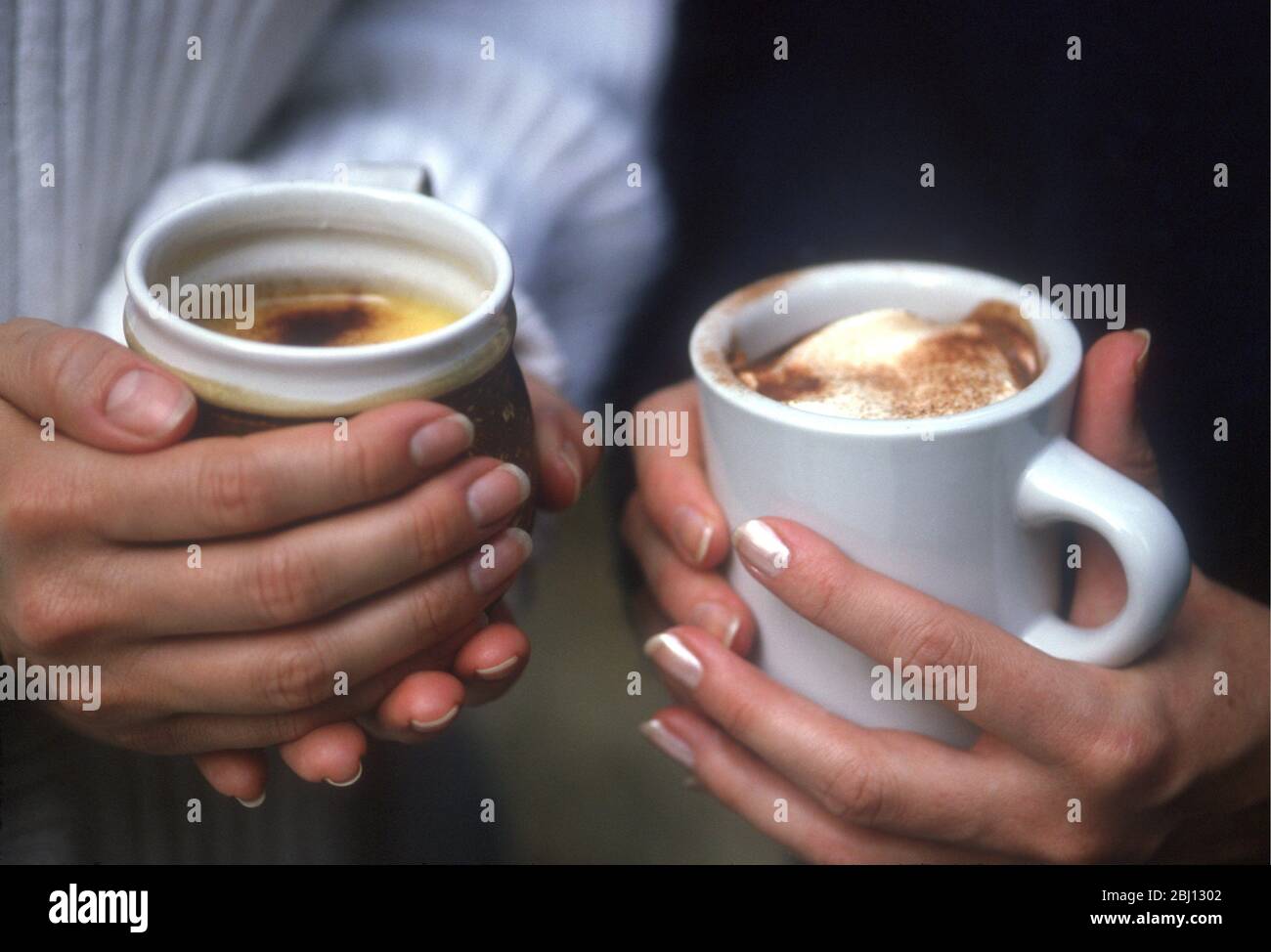 Bevande calde in mano - condite con latte schiumoso e polvere di cioccolato - Foto Stock