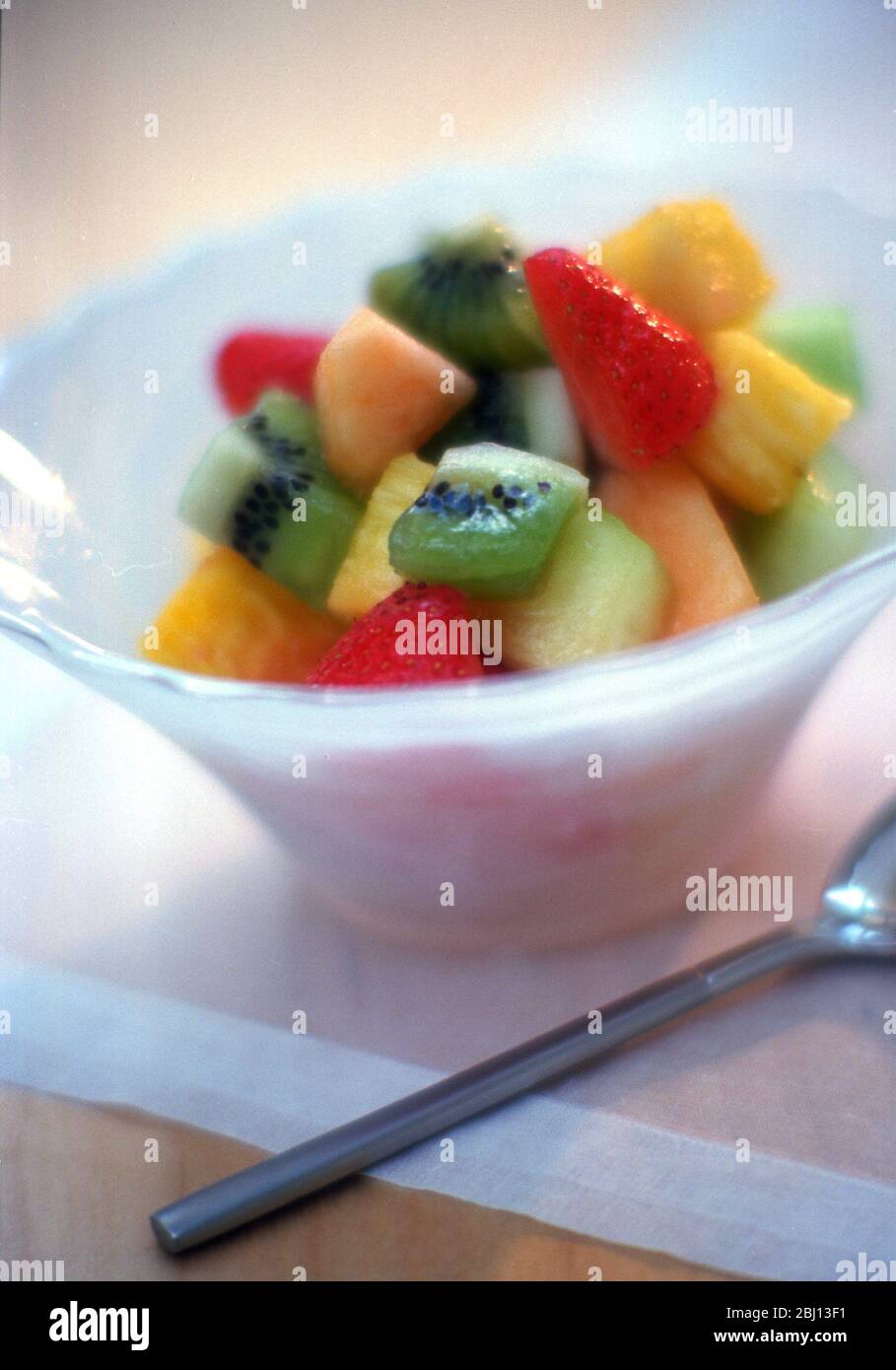 Macedonia di frutta fresca in una ciotola di vetro bianco - Foto Stock