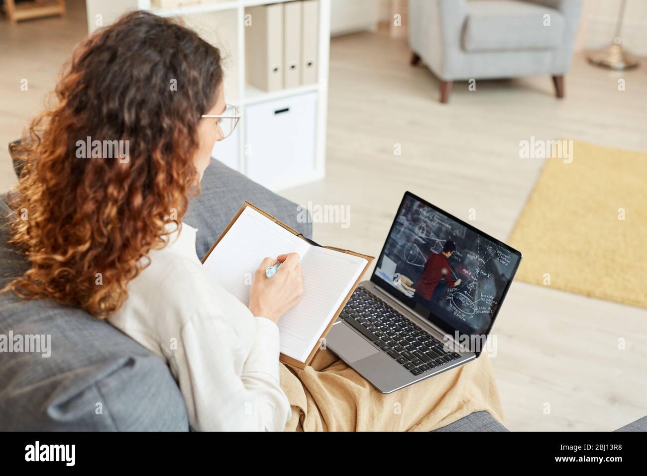 Donna d'affari concentrata seduta sul divano prendere appunti mentre si guarda una videoconferenza Foto Stock