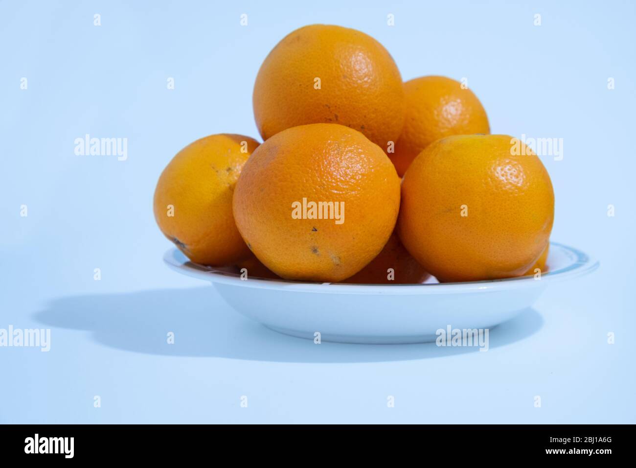 Molte arance ricche di vitamina C sono poste in un piatto di ceramica su sfondo bianco. Foto Stock