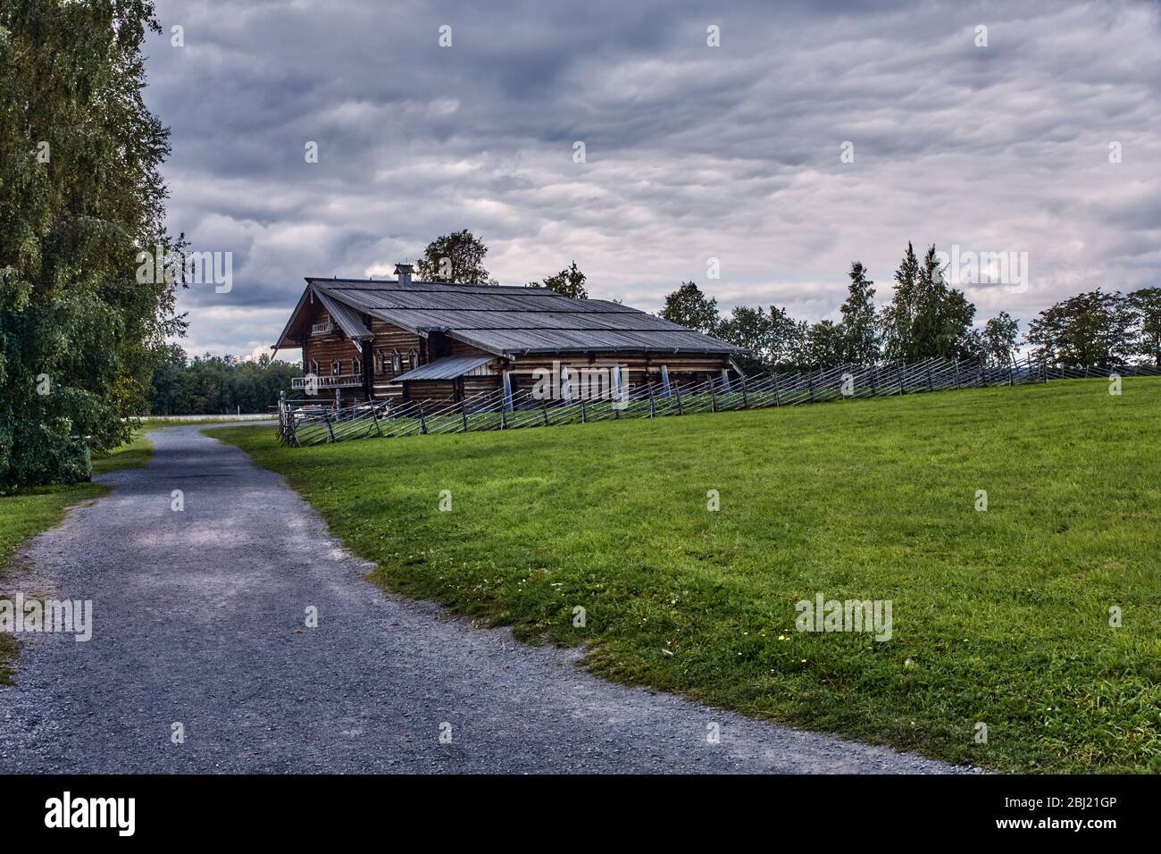 Casa di villaggio di legno. Portico visibile, finestre, tetto. La casa è circondata da alberi. Intorno alla casa è una recinzione di legno fatta di pali Foto Stock