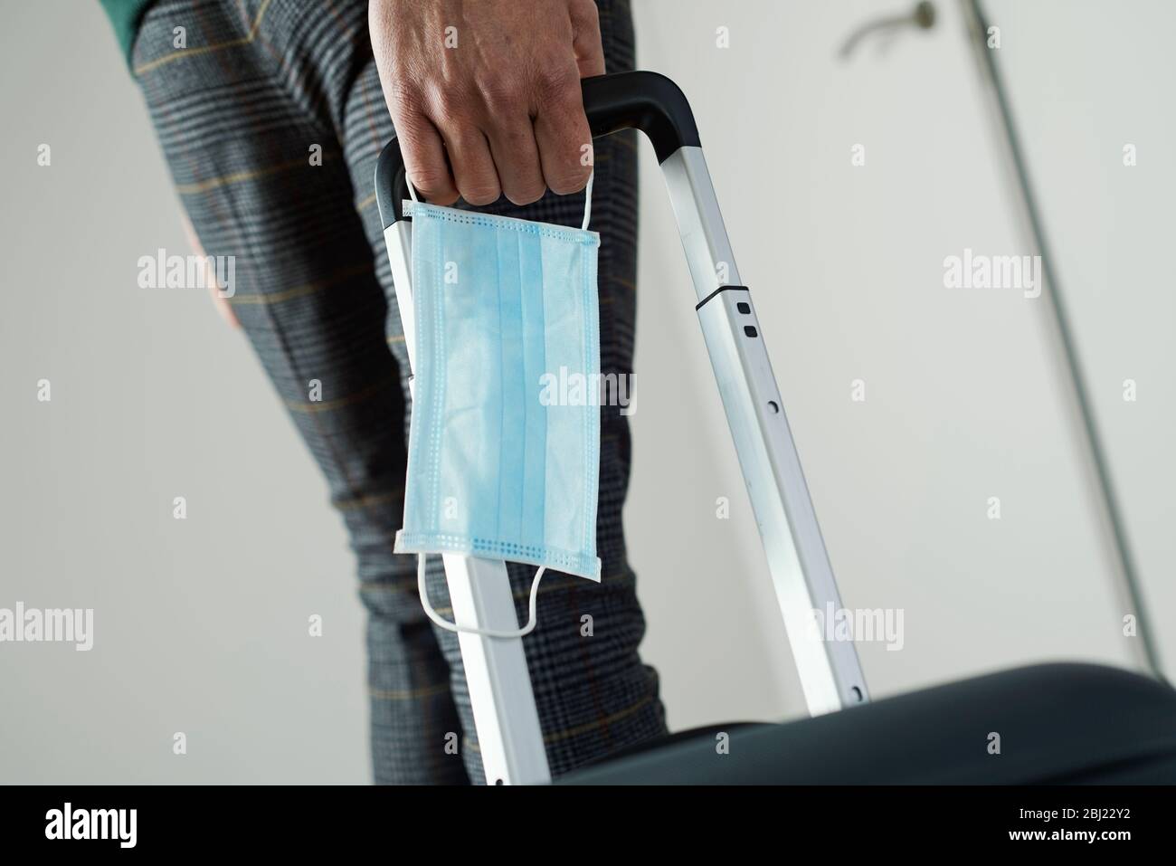 primo piano di un giovane, con una maschera chirurgica in mano, tirando una valigia per il suo manico telescopico Foto Stock